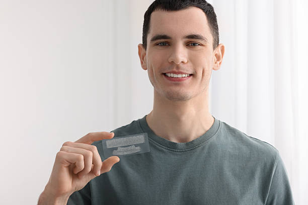 istock Young man with whitening strips on light background. Space for text 2203910585