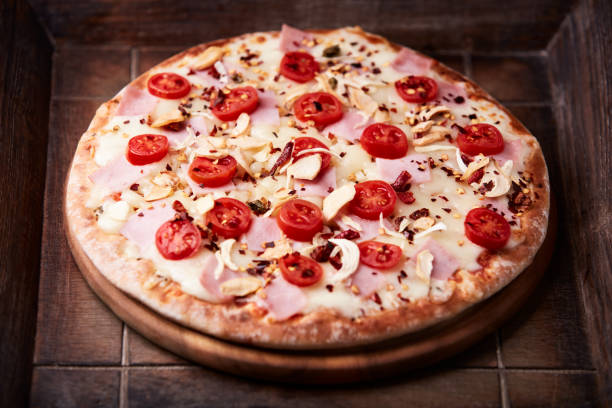 istock Pizza with ham, cherry tomatoes and mozzarella cheese. Wooden background. Soft focus. Close up. 2203910712