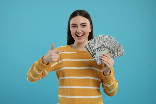 istock Happy woman pointing at dollar banknotes on light blue background 2203914641