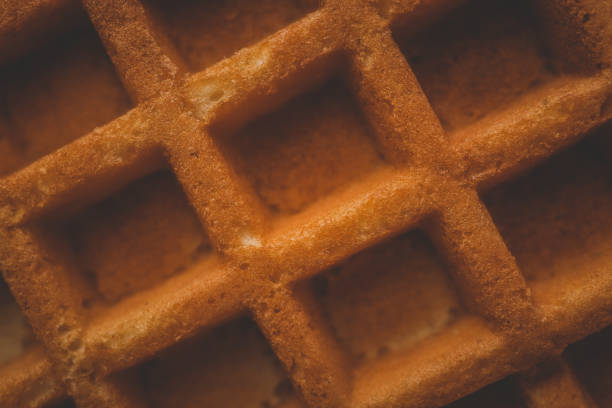 Golden-brown crispy waffles in a close-up shot. Detailed texture with a crisp outer layer and soft interior. Freshly baked breakfast food with a warm and inviting appearance.