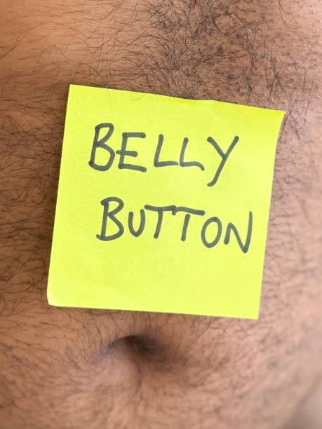 istock Close-up image of  'Belly Button' phrase written in black felt tip pen on yellow, sticky note stuck on hairy, fat belly of unrecognisable, overweight man, focus on foreground 2203919566
