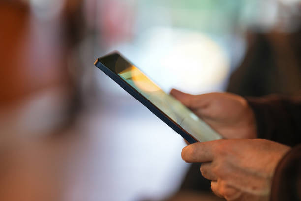 A close-up of a person holding a tablet with a softly lit background. The screen reflects ambient light, creating a warm and inviting atmosphere.