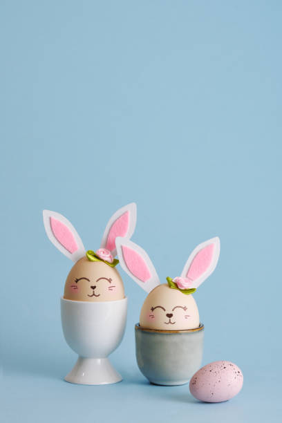 istock Cute Easter eggs bunny in egg holders on blue background. Vertical postcard. Place for your text 2203926782