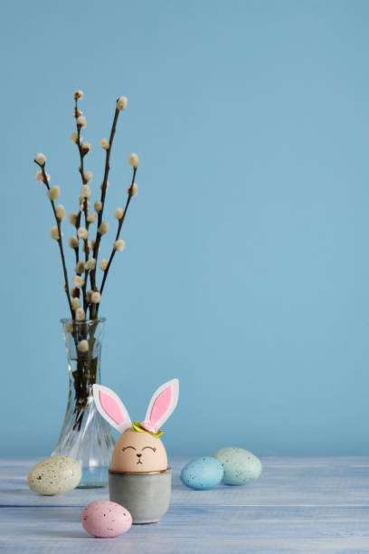 istock Easter bunny eggs in egg holder on blue background. Multicolored eggs and sprigs of willow. Place for your text 2203926953