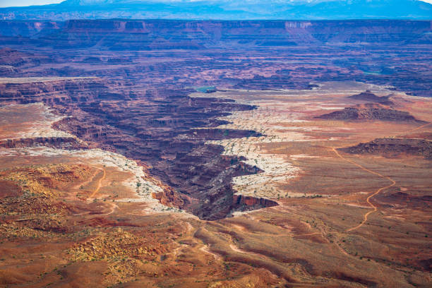 Aerial view of Canyonlands National Park in Utah, showcasing deep canyons, dirt roads, rugged terrain, and winding riverbeds. This dramatic desert landscape captures the vast beauty of the American Southwest’s geological formations and untouched wilderness.