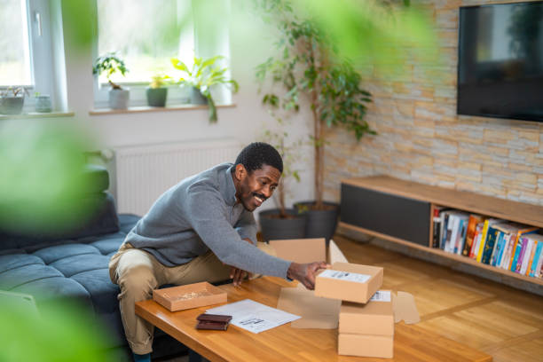 istock Smiling Black Man Packing Shipment Boxes in Cozy Home Setting 2203931810