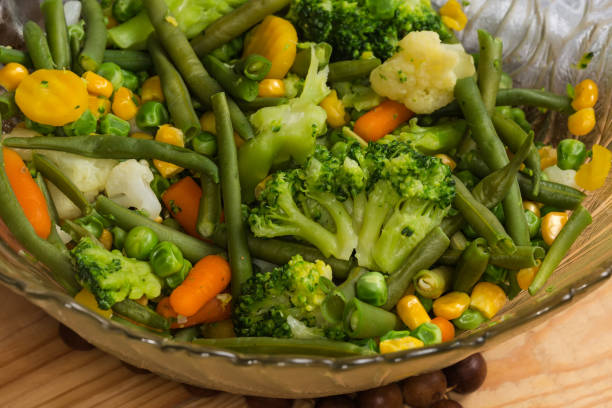 Mixture of the pieces of different boiled vegetables in the glass salad bowl, fragment close-up in selective focus