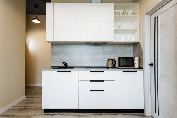 The kitchen features stylish white cabinets, a convenient microwave, a modern kettle, and a functional sink that offers both utility and elegance to the overall design of the space