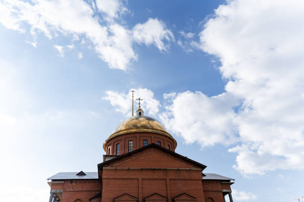 A sturdy brick building features a large dome atop its structure, beautifully contrasting with a serene blue sky dotted with fluffy clouds, creating a picturesque and visually appealing view