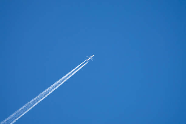 istock Airplane in a blue sky without clouds. The airplane has a flight trail behind it. 2203939920