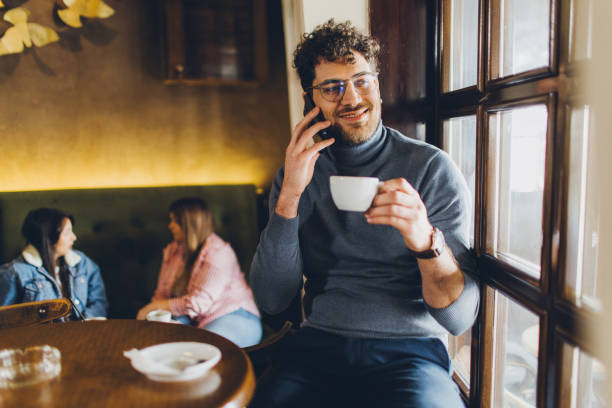 istock Smiling young man talking on phone in coffee shop 2203942397