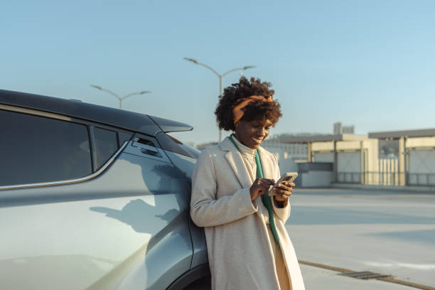 istock Woman leaning on a car using her smartphone in a modern outdoor setting 2203950367