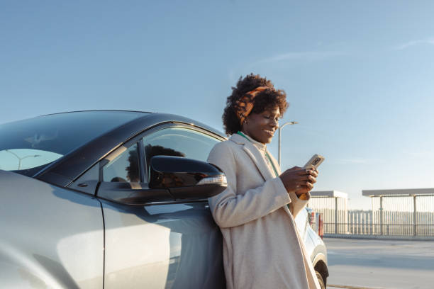istock Young woman leaning on car while texting on smartphone outdoors 2203950368