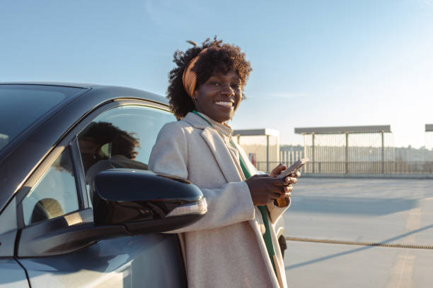 istock Young woman leaning on car while texting on smartphone outdoors 2203950376