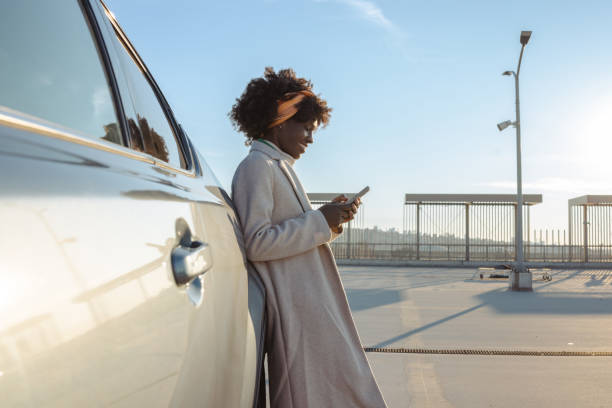 istock Woman leaning on car using smartphone while enjoying sunshine outdoors 2203950412
