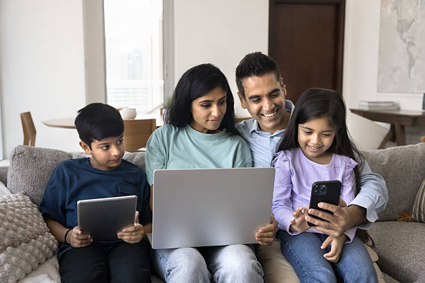 istock Indian family using diverse modern gadgets seated on couch 2203953913