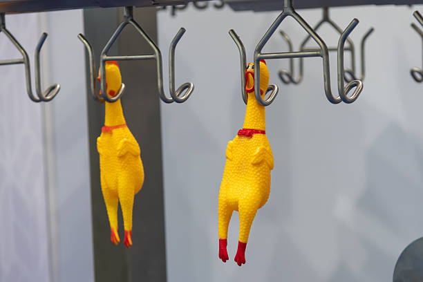 Two yellow rubber chickens with red accents dangle from metal hooks in a lively exhibition environment. The quirky display attracts attention and adds humor to the event atmosphere.