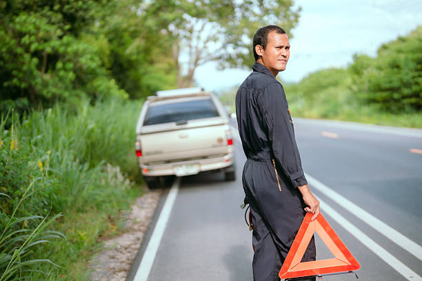 istock Man on roadside holds warning triangle after car breakdown during daylight near a lush green landscape 2203965753