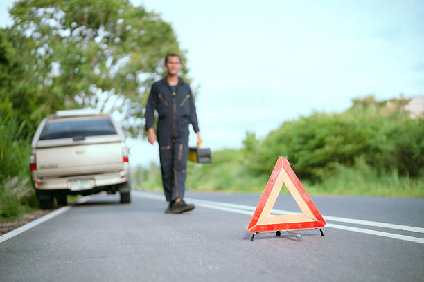 Alava province, Spanish Basque Country. Emergency triangle on the road marking a broken-down car, with a man using his mobile phone to request roadside assistance.