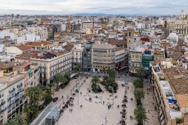 Valencia, Spain - February 25, 2025: Plaza de la Reina, bustling historic city square surrounded by traditional European architecture. Palm trees and small groups of people populate the open plaza.