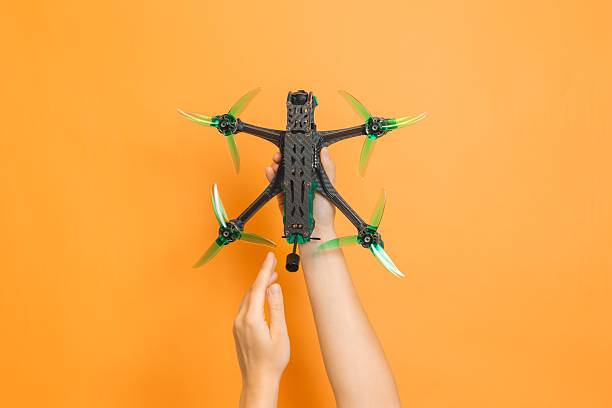 istock Hands holding professional modern drone with camera on orange background 2203973146