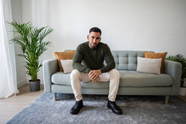 istock Young man sitting on sofa in modern apartment living room 2203976626