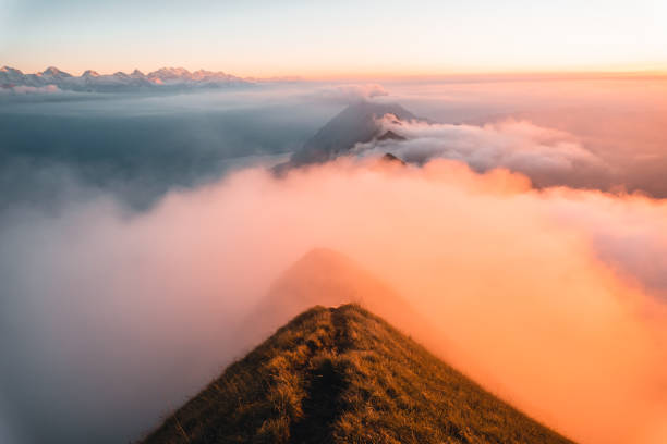 View down narrow trail on mountain ridge above clouds at sunrise, Valais, Swiss Alps