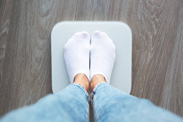 A person wearing white socks and jeans standing on a digital scale, viewed from above, symbolizing weight measurement and health monitoring