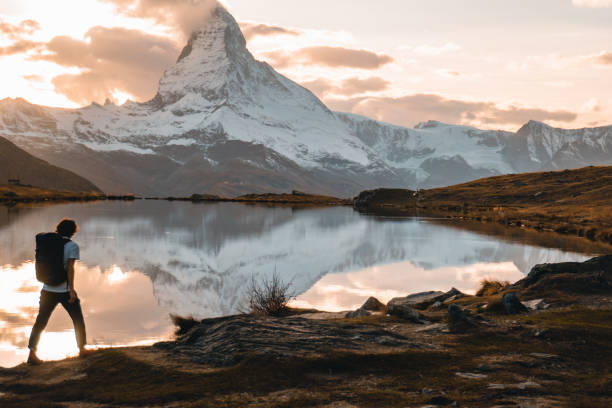 Young man hikes along Stellisee lakeshore in alpine below Matterhorn Peak at sunrise, Valais, Swiss  Alps