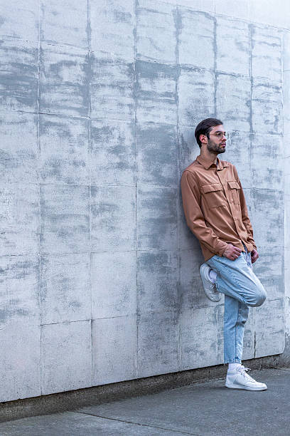 istock Thoughtful young man leaning against concrete wall waiting 2203987436