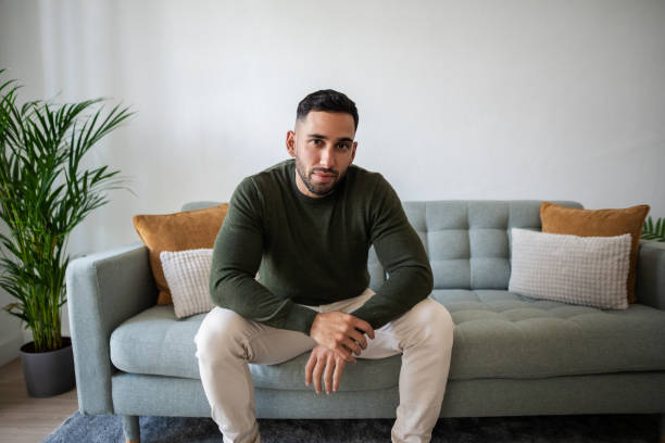 istock Young man sitting on sofa in modern apartment living room 2203988305