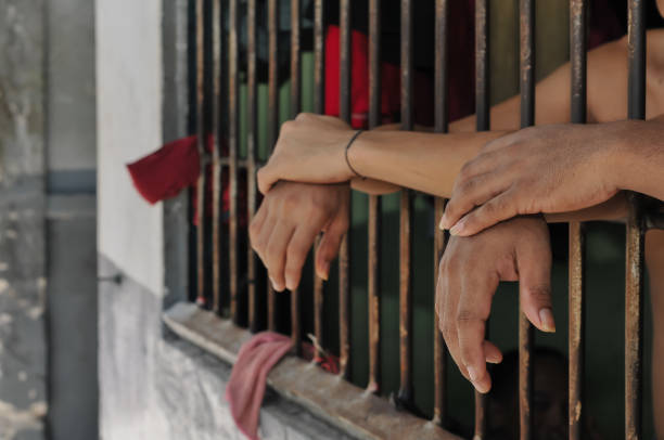 istock prisoner's hands behind bars with black background 2203988420