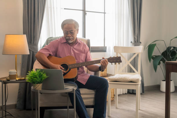 istock Asian senior retired old male man  with beard Senior man study online learning playing guitar from laptop at home 2203989331