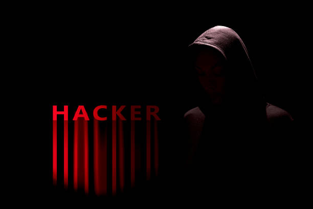 istock Dark silhouette of a hacker in a hoodie with red glowing hacker text 2203991036