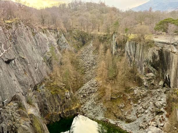 istock A deep abandoned slate quarry with a green pool at the base, surrounded by rugged rock formations. 2203992083