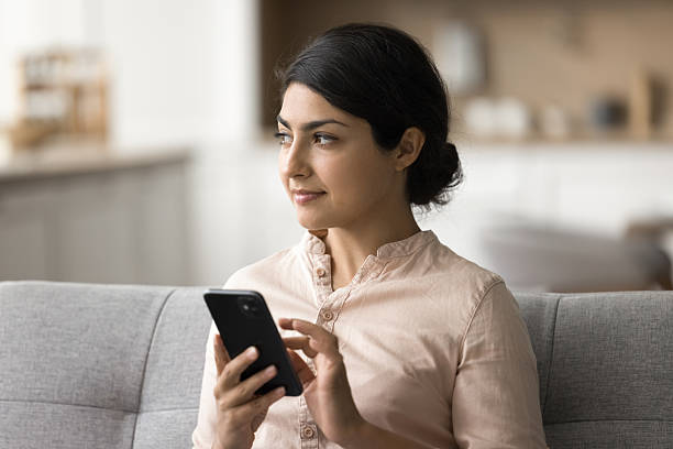 istock Pensive young lady resting on sofa at home holding cellphone 2203993007