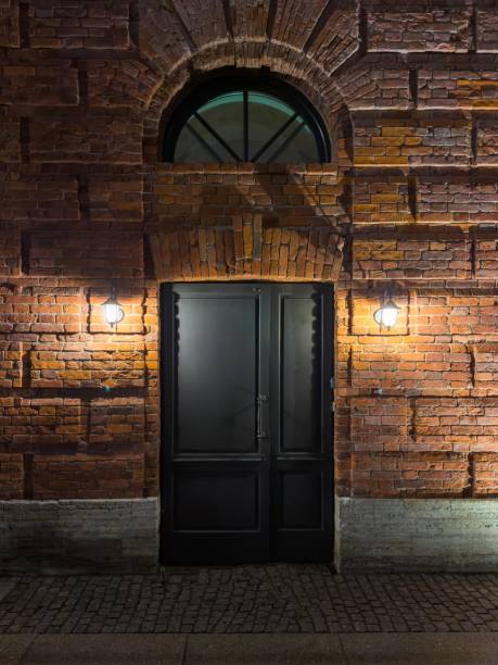 istock Elegant black door set in a historic brick wall illuminated at night 2203995180