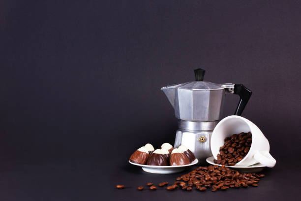 istock Espresso maker, chocolate truffles on small plate, and an overturned mug spill coffee beans on a dark surface. The mood is intimate and relaxing 2204005229