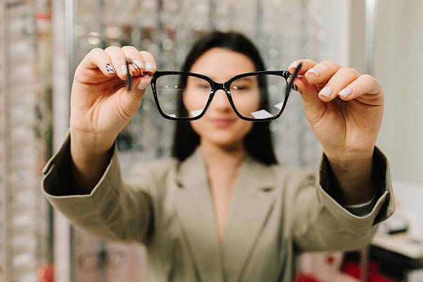 istock Eyesight correction. Stand of eyeglasses with different frames in the optical store. Customer chooses eyeglasses with clear lenses from the shelf. 2204008012