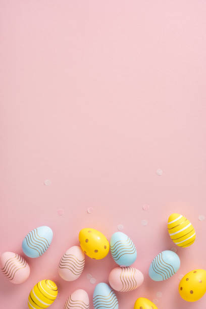 istock Decorated vertical Easter eggs in yellow, blue, and pink placed on a light pink background 2204010882