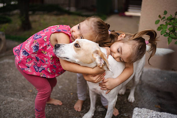 Two little sisters are embracing their mixed-breed dog, showing love and affection in their backyard