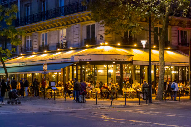 Locals and torurists enjoying the evening sun at the iconic Café Fleurus with its classic orange and yellow awnings on a hot summer afternoon in the streets of Paris, France