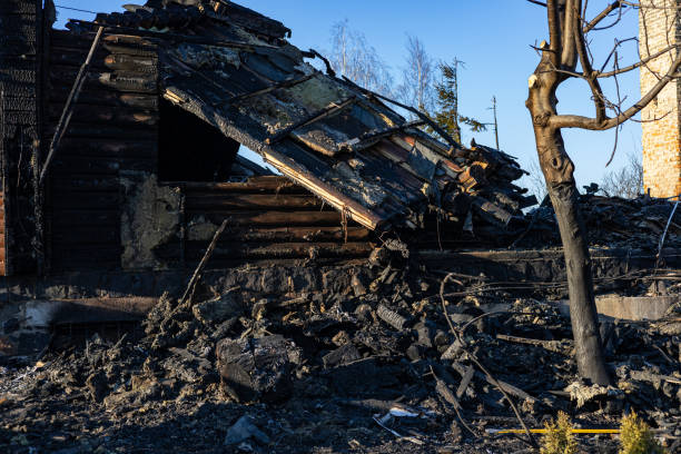 istock A burned-down wooden structure stands in ruin, surrounded by charred debris and ashes, with a clear sky overhead 2204016138