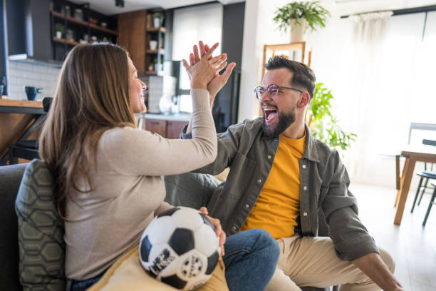 istock Excited couple cheering while watching soccer match at home 2204020746