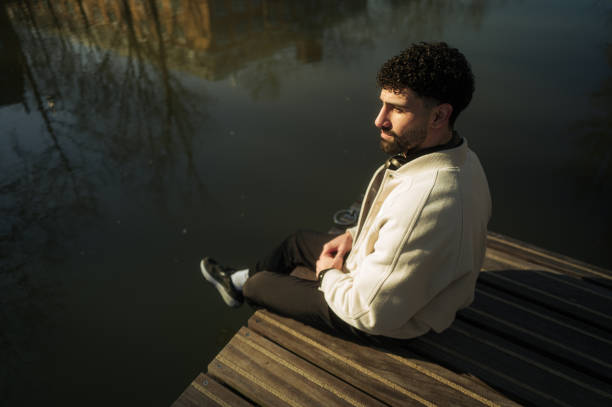 Stylish man enjoying a peaceful moment by the water, sitting on a wooden dock