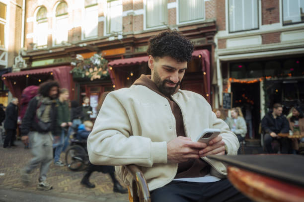 istock Young man using smartphone while sitting at outdoor cafe in amsterdam 2204022304