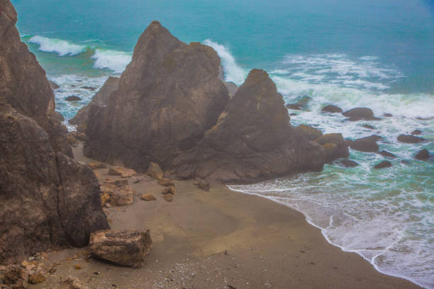 Golden sandy cliffs overlook a pristine shoreline where gentle waves lap against the beach. A clear blue sky making a serene landscape on the Pacific California coast Route US 101.