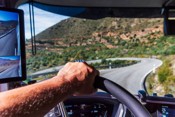 istock Driver's hand firmly gripping the steering wheel on a mountain descent with a sharp curve. 2204030620