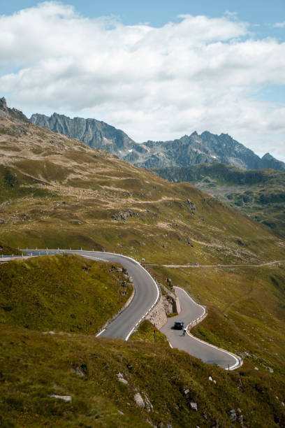 istock Road biker rides up high mountain pass, distant view, Swiss Alps 2204038347