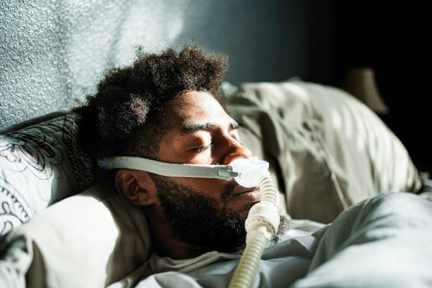 istock Athletic Young African American Man in His Twenties Sleeping Peacefully Using a CPAP Machine (contenuous positive air pressure) in a Dark Bedroom 2204039216